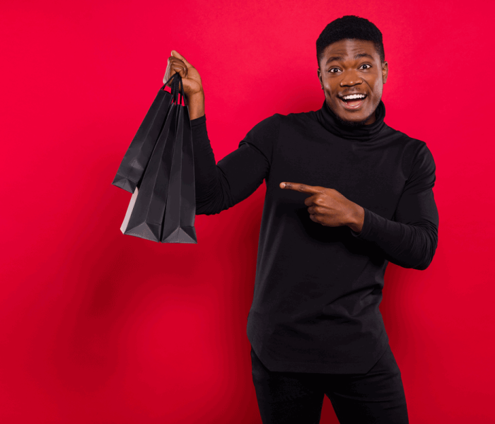 Portrait of attractive trendy cheerful guy buying demonstrating gifts holiday isolated over vibrant red color background